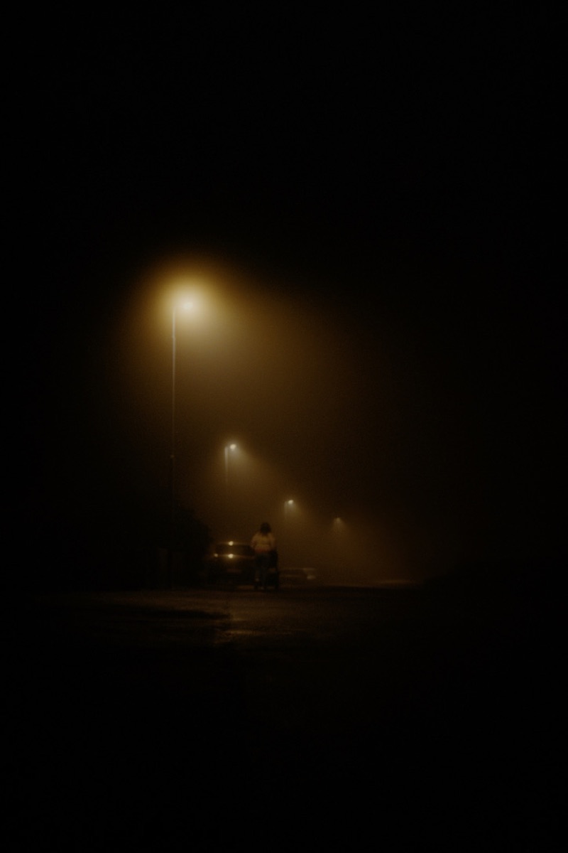 Lone figure standing under street lights in dense fog