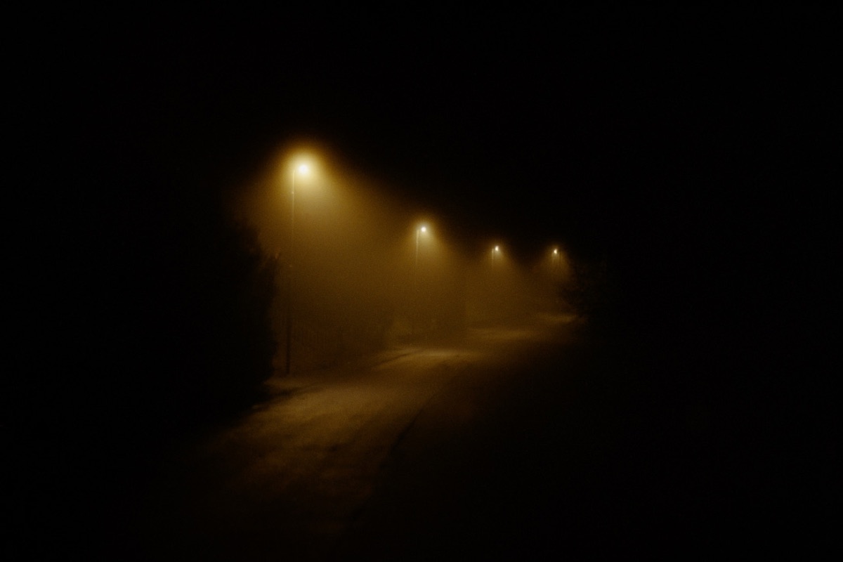 Foggy road lit by sodium street lamps receding into darkness